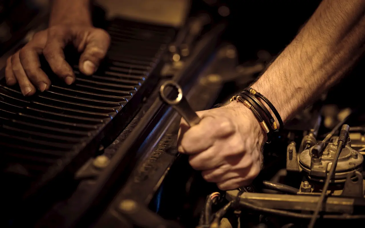 Mains d'un mécanicien serrant un écrou avec une clé plate dans un compartiment moteur