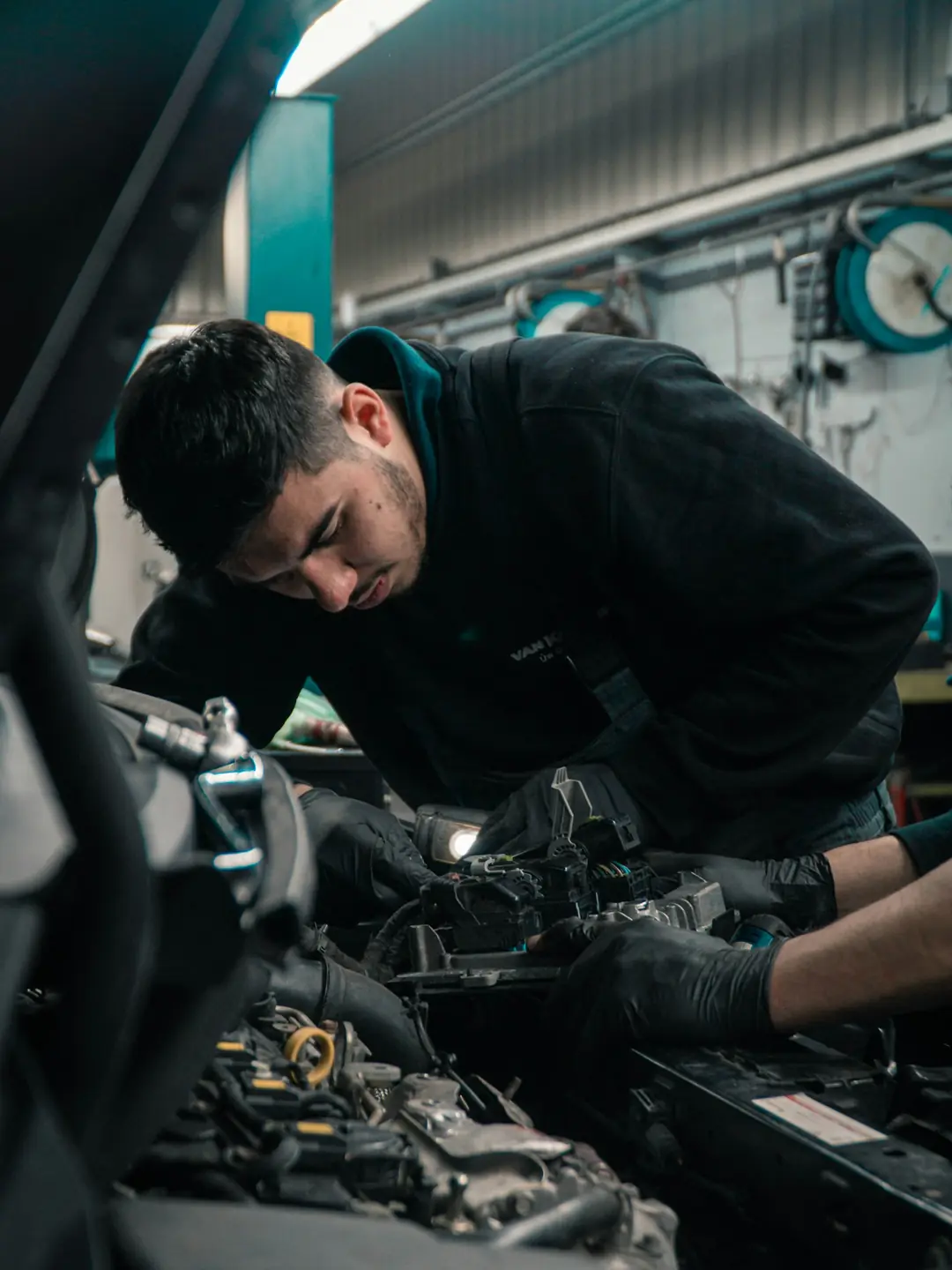 Mécanicien penché sur un moteur dans l'atelier, lampe d'inspection à la main